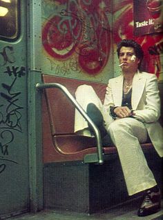 a man sitting on top of a bench next to a wall covered in grafitti