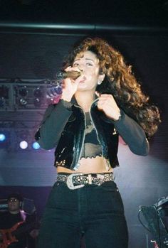 a woman standing on top of a stage holding a microphone in her hand and singing