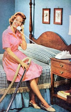 a woman is sitting on her bed talking on the phone while holding a vacuum cleaner