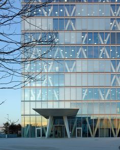 an office building with glass windows and trees in the foreground on a sunny day