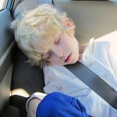 a young boy sleeping in the back seat of a car with his head resting on an arm rest