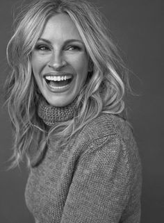 a smiling woman with long blonde hair wearing a gray sweater and turtleneck neck sweater