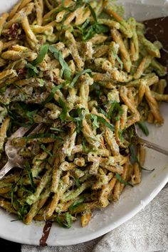 a white plate topped with pasta covered in pesto sauce and green onions next to a fork