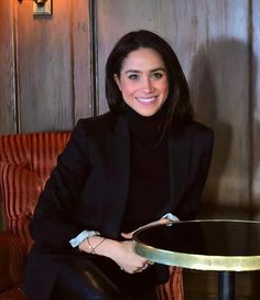 a woman sitting at a table with a smile on her face and black suit jacket