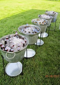 four metal buckets filled with drinks sitting on top of a grass covered field next to an ice chest