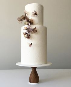 a three tiered white cake with flowers on the top and bottom, sitting on a wooden stand