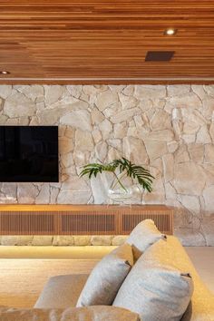 a living room with couches and a flat screen tv mounted on the stone wall