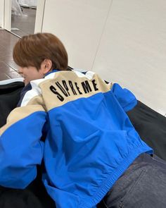 a young boy sitting on the floor with his back turned to the camera, wearing a blue and white jacket