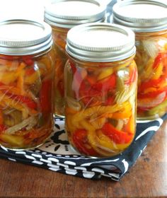 four jars filled with pickled vegetables on top of a black and white cloth covered table