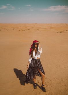 a woman standing in the desert wearing a red bandana and black polka dot skirt