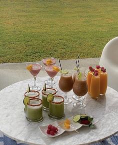 a table topped with glasses filled with different types of drinks next to a bowl of fruit