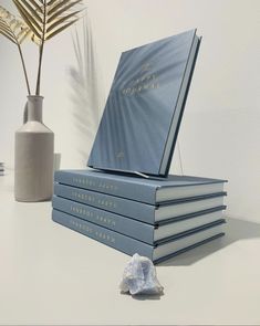 a stack of blue books sitting on top of a white table next to a vase