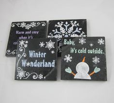 four coasters decorated with snowflakes and sayings on black slate tiles,