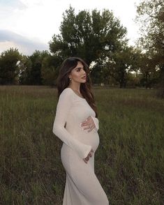 a pregnant woman in a white gown poses for a photo