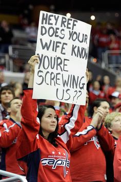 a woman holding up a sign in front of her head at a hockey game with other people watching