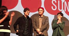 three young men standing on stage with one holding his hand to his mouth and the other looking at him