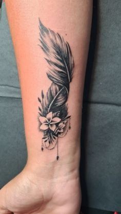 a woman's arm with a feather and flower tattoo on it