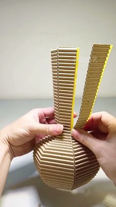 two hands are holding an origami vase made out of cardboard and yellow tape