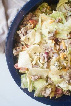 a blue bowl filled with lettuce, meat and cheese salad on top of a white table