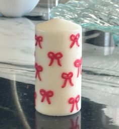 a white candle with red bows on it sitting on a black table next to a glass bowl