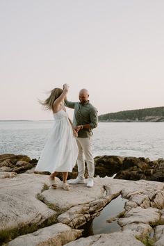 a man and woman dancing on rocks by the water