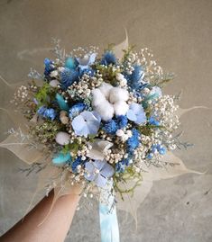 a bridal bouquet with baby's breath and blue flowers is being held by someone