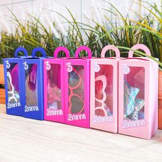 four different colored boxes with sunglasses in them on a table next to potted plants