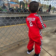 a young boy standing next to a fence wearing a red and black track suit with checkered sides