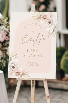 a baby shower sign on an easel with flowers in the background and greenery