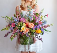 a woman holding a vase filled with lots of flowers