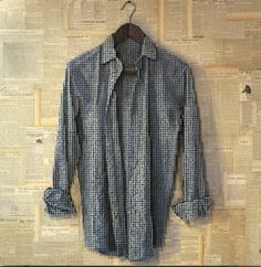 a blue shirt is hanging on a wall with newspaper pages in the background and a wooden hanger attached to it