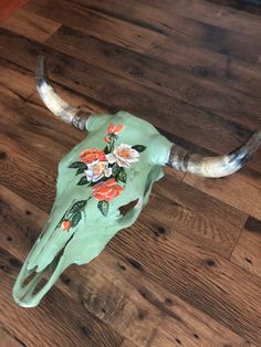 a cow skull with flowers painted on it's side sitting on a wooden floor