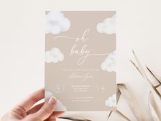 a person holding up a baby shower card with clouds in the sky on it's back