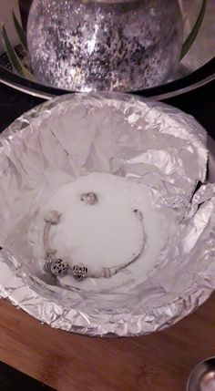 an aluminum foil covered dish sitting on top of a wooden table next to a silver pot