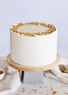 a white cake sitting on top of a wooden stand next to a bowl of nuts