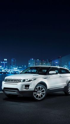 a white range rover parked in front of a city at night