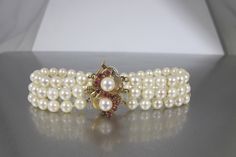 Stunning vintage triple strand Akoya Pearl Bracelet with a gorgeous 14K Yellow Gold Double flower Ruby Clasp with safety lock.  The three strands are held together by two 14K Yellow gold stabilizer bars. This gorgeous bracelet is perfect for that special day or as a gift for that special someone or for yourself.   Excellent condition with all stones present and secure.  Measures 8 inches long. Pearls are 5.2mm. Clasp is .75 inch from top to bottom.  Hallmarked 14K G. Feel free to contact me with any questions. Elegant Double Strand Bracelets For Formal Occasions, Elegant Double Strand Bracelet For Formal Occasions, Elegant Formal Double Strand Bracelet, Elegant Multi-strand Bracelet For Formal Events, Elegant Multi-strand Jubilee Bracelet Jewelry, Ruby Flower, June Birthstone, Akoya Pearls, Gorgeous Bracelet