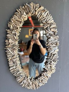 a woman taking a selfie in front of a mirror made out of driftwood