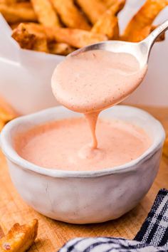 a spoon full of sauce being poured into a bowl with french fries in the background