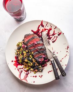 a white plate topped with meat and vegetables next to a glass of red wine on top of a table