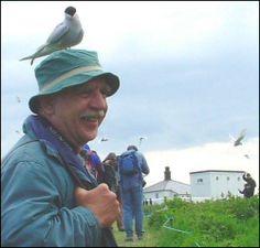 a man with a bird on his head standing in front of some birds flying above him