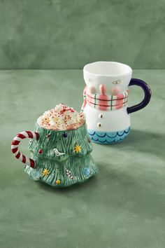 two coffee mugs sitting next to each other on a green counter top with candy canes