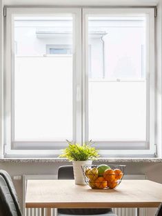 a bowl of fruit sitting on top of a wooden table next to a window covered in blinds