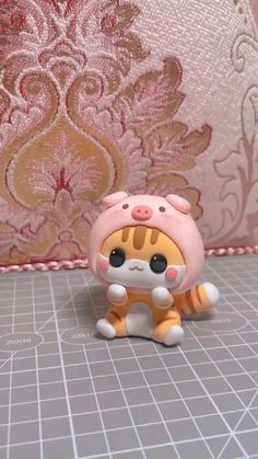 a small toy cat sitting on top of a tile floor next to a pink wall