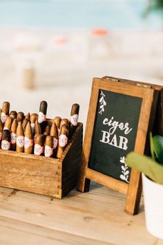 a wooden crate filled with cigars next to a chalkboard sign and potted plant