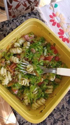 a yellow bowl filled with pasta salad on top of a counter next to a fork