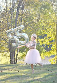 a woman in a tutu skirt is holding a balloon with the number 55 on it