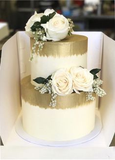 two tiered wedding cake with white flowers on top and gold stripes around the edges