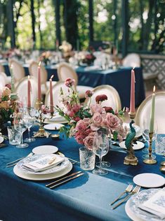 the table is set with blue linens and white plates, silverware, and pink flowers