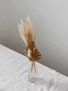 a vase with some dried plants in it on a white sheeted tablecloth,